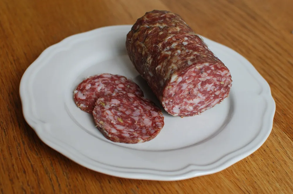 Finocchiona, salami toscan au fenouil, entier et en tranches sur une assiette blanche posée sur une table en bois