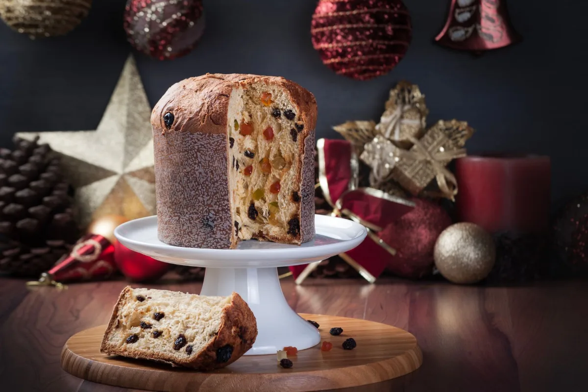 Panettone entier sur un présentoir, avec une part coupée posée devant et des boules de Noël autour