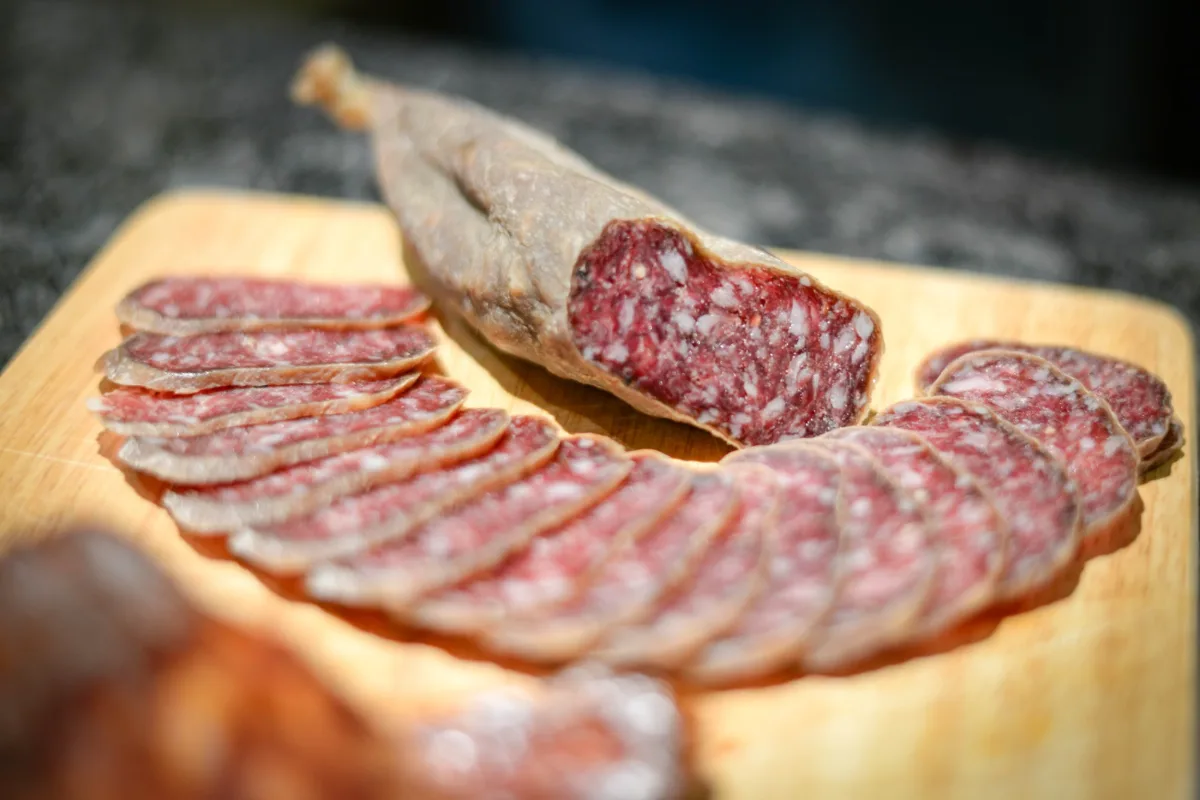 Salami italien coupé en tranches fines sur une planche en bois, avec un morceau de saucisson entier